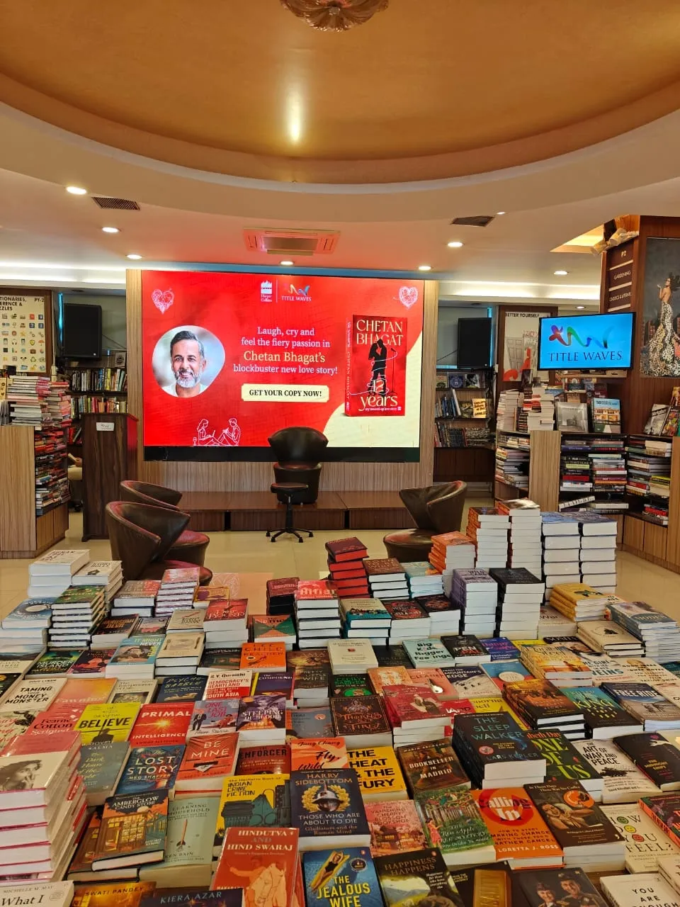 An in-store screen and stacked table displays promoting Chetan Bhagat’s novel 12 Years at a Title Waves bookshop.